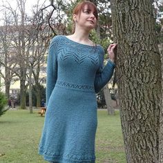 a woman standing next to a tree wearing a blue knitted dress and tights