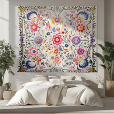 a large tapestry hanging on the wall above a bed in a room with potted plants