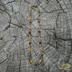 a yellow and black beaded necklace sitting on top of a piece of tree trunk