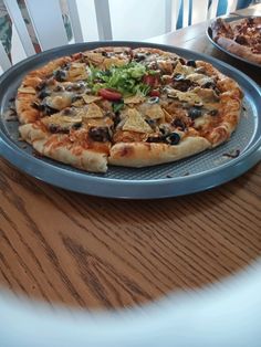 a pizza sitting on top of a metal pan covered in toppings next to a wooden table