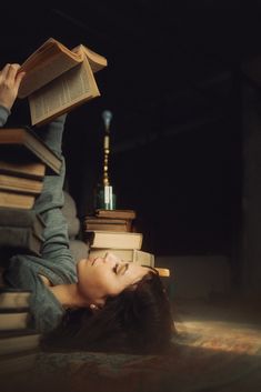 a woman laying on the floor reading a book and leaning up against a stack of books