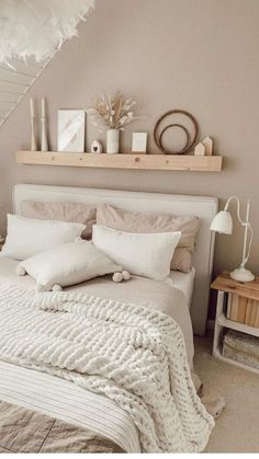 a white bed sitting under a window next to a wooden shelf filled with pictures and candles