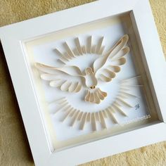 a paper sculpture of a dove with wings in a white frame on a beige carpet