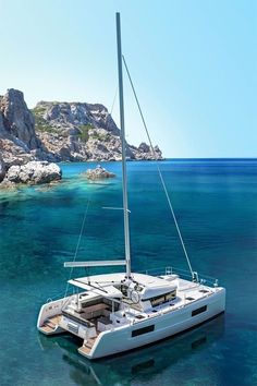 a catamaran sailing in the blue water near an island with rocks on it