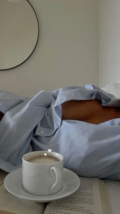 a person laying in bed next to a cup of coffee