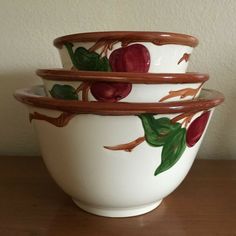 three bowls with fruit painted on them sitting on a wooden table next to a wall