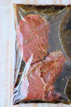 two raw meats in a plastic bag on a wooden table with seasoning sprinkled around them