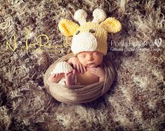 a baby wearing a knitted giraffe hat laying on top of a blanket