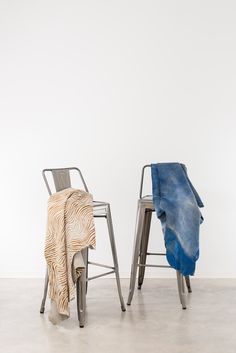 two metal chairs sitting next to each other on top of a cement floor in front of a white wall