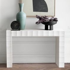 a white table with two vases on top of it and a painting behind it