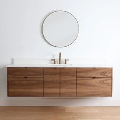 a bathroom vanity with two sinks and a round mirror on the wall above it, in front of a white wall