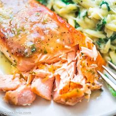 a plate with salmon, pasta and spinach covered in sauce on it next to a fork