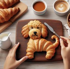 a person is decorating a dog shaped pastry on a wooden board with coffee and croissants