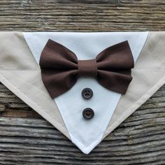 a brown bow tie and two buttons on a white pocket square with a wooden background