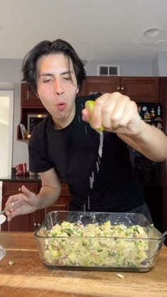 a man is making a salad in the kitchen with his hands and spoons sticking out