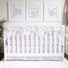 a white crib with pink and purple floral bedding in front of three framed pictures