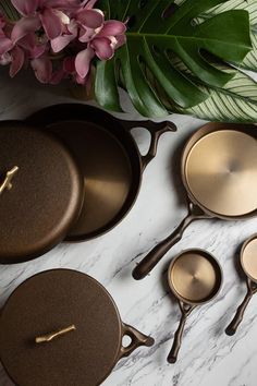 four pots and two pans on a marble counter top with flowers in the background