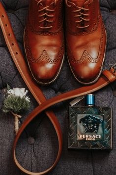 a pair of brown shoes sitting on top of a bed next to a bottle of cologne