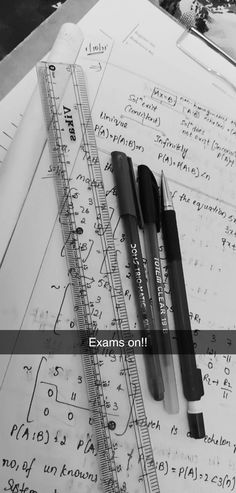 two pens and ruler on top of some paper with calculations in the background that says, exam online