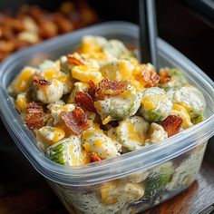 a plastic container filled with pasta salad next to another container full of cheese and bacon