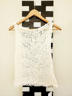 a white knitted tank top hanging on a wooden hanger next to a black and white striped wall