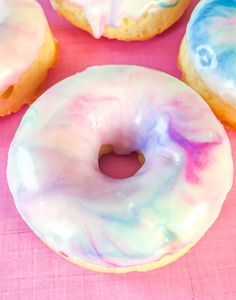 there are four donuts with icing on the pink tablecloth and one is missing