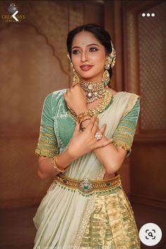 a woman in a green and gold sari with her hands on her chest, posing for