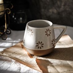 a white coffee cup sitting on top of a table next to an open book and candle