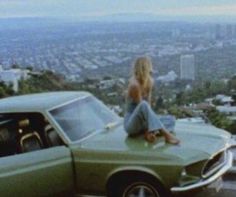 a woman sitting on top of a green car in front of a cityscape