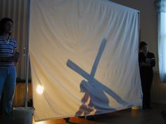 two people standing in front of a white backdrop with a shadow of a cross on it