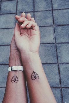 two people holding hands with tattoos on their wrists