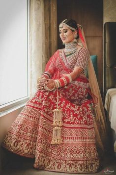 a woman in a red and gold bridal gown sitting on a bed next to a window