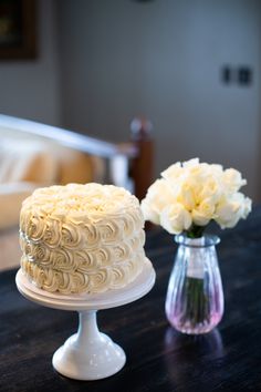 a white cake sitting on top of a table next to a vase filled with flowers