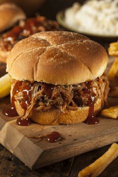 pulled pork sandwich with barbecue sauce and french fries on a cutting board - stock photo - images