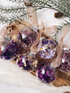 six ornaments are sitting on a wooden board with pine branches in the background and snow flakes all around them