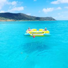 two people in an inflatable boat floating on the blue water with mountains in the background