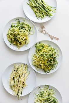 three white plates filled with zucchini noodles and green beans next to silverware