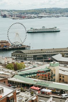 a ferris wheel is in the distance over some buildings and water with cars on it