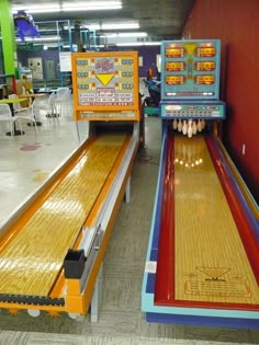 two bowling lanes in a building with people sitting at the tables and one person standing next to them