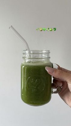 a hand holding a mason jar with a green smoothie inside and a straw in it