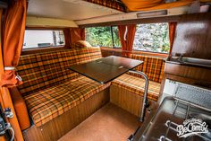 the inside of a camper with orange curtains and checkered couches, table and sink