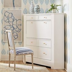 a white dresser sitting next to a blue and white flowered wallpaper in a living room