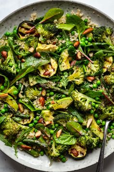 a white bowl filled with broccoli, peas and other veggies next to a fork