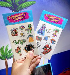 someone holding up two temporary tattoos in front of a blue wall with cartoon characters on it