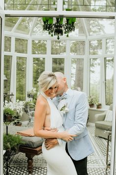 a man and woman standing next to each other in front of a glass house with plants