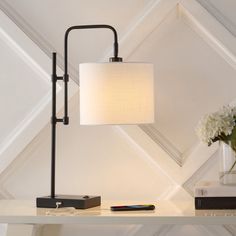 a table with a lamp and some books on it next to a vase filled with flowers