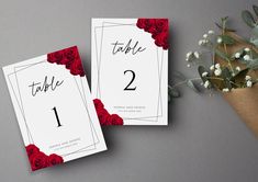 two red roses are sitting next to each other on top of a table number card