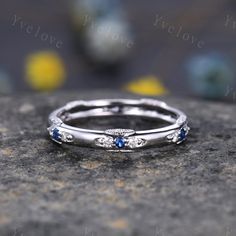 a silver ring with blue sapphire stones on top of a gray rock in front of yellow flowers