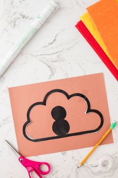 a paper cut out of a cloud with scissors and markers on the table next to it