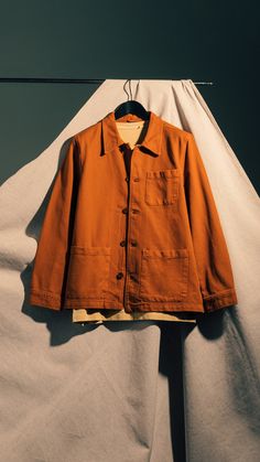 an orange jacket is hanging on a clothes line with white sheets in the back ground